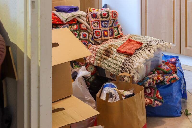 Hoarded room with boxes, bags and blankets piled against a wall before a hoarding and squalor clean up