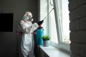 Worker in a protective suit and respirator spraying a window frame inside a home