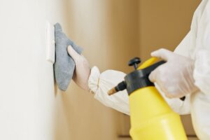 Gloved hand wiping a light switch with a cloth during meth clean up remediation