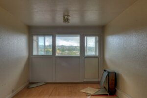 Empty, run down living room with marked walls and debris on the floor